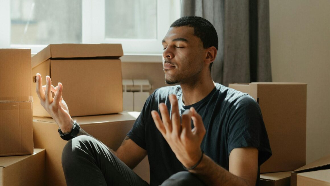 A person meditating next to a pile of cardboard boxes